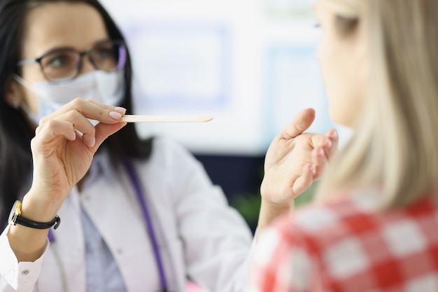 Doctora examinando la garganta del paciente con diagnóstico y tratamiento de primer plano de espátula de madera