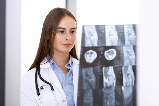 Foto doctora examinando una imagen de rayos x mientras está de pie cerca de la ventana en el hospital. cirujano u ortopedista en el trabajo. conceptos de medicina y atención médica.