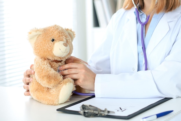 Doctora examinando a un paciente de oso de peluche con estetoscopio. Concepto de atención médica para niños