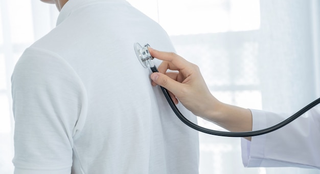 Doctora examinando la salud de los pacientes masculinos con un estetoscopio.