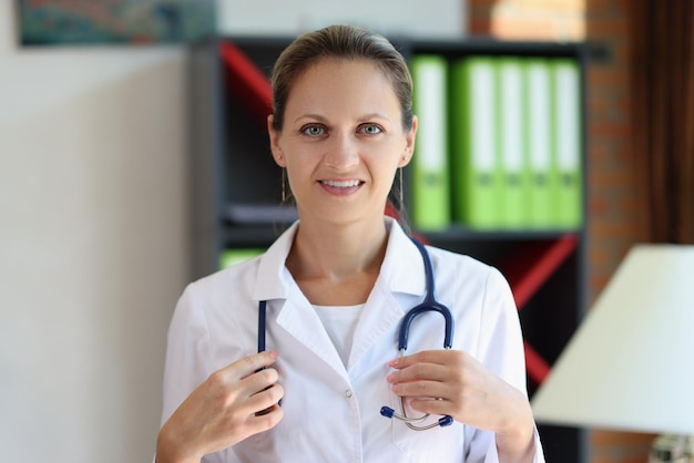 Doctora feliz con estetoscopio mirando a la cámara en el consultorio médico