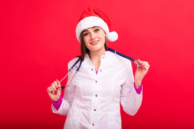 Una doctora feliz con un sombrero de Santa Claus posa en el estudio con un fondo rojo