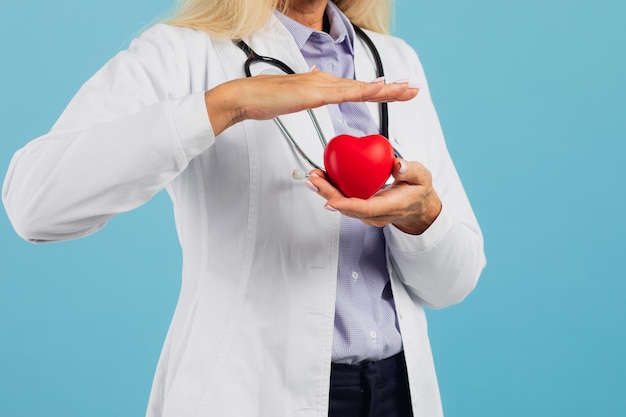 Doctora en gafas con estetoscopio sosteniendo el corazón en el fondo azul con espacio de copia