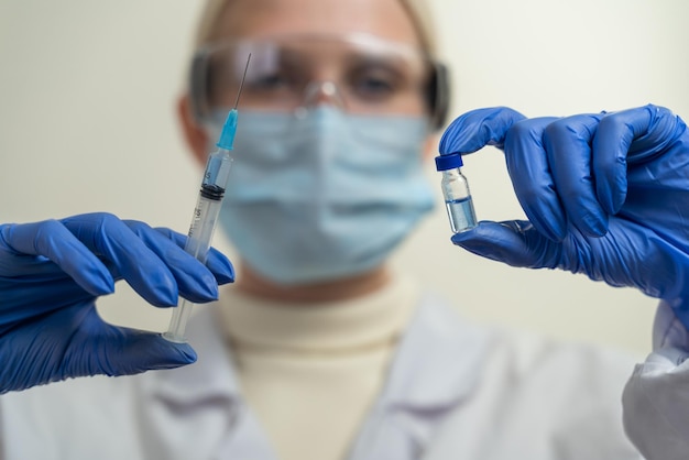 Una doctora con gafas y guantes médicos sostiene una jeringa y una ampolla con una vacuna frente a ella. Convocatoria de vacunación obligatoria de la población. Ciencia y medicina.