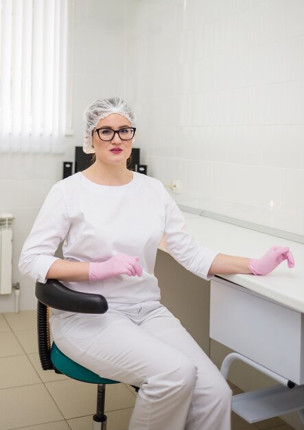 Una doctora con gafas y un uniforme blanco se sienta en una silla en la oficina de la clínica.