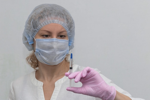 Una doctora, con guantes y una máscara, llena una jeringa con medicamento, de cerca. Vacunación Covid-19