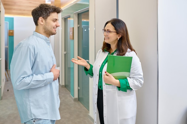 Doctora hablando con un paciente masculino. Médico explicando algo a un joven en el corredor