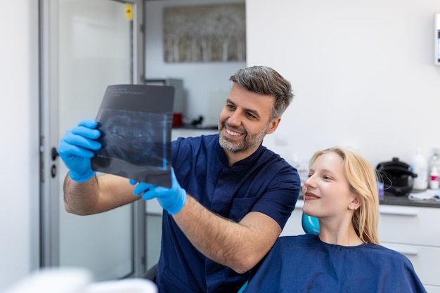 Doctora hablando con su paciente y enseñándole una radiografía Concepto de dentista de mujer sentada en una silla dental mientras su dentista lee una radiografía