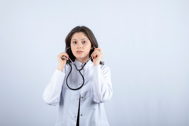 Doctora joven con estetoscopio para comprobar el pulso en la pared blanca.