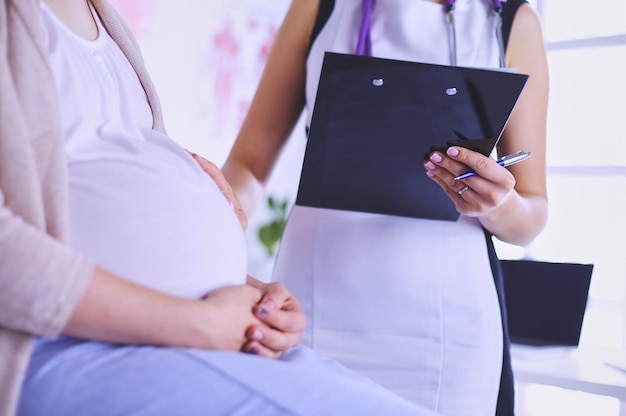 Doctora joven con estetoscopio y tableta hablando con una mujer embarazada en el hospital