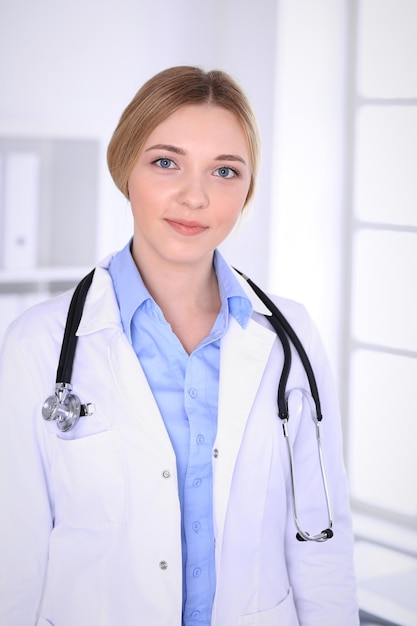 Doctora joven en el trabajo en el hospital mirando a la cámara. Se ve bien la blusa color caqui de terapeuta. Concepto de medicina y salud.