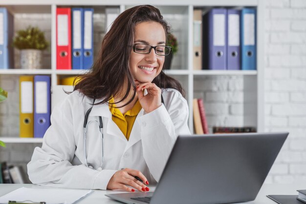 Doctora joven en el trabajo en el hospital mirando el monitor de la computadora portátil de escritorio