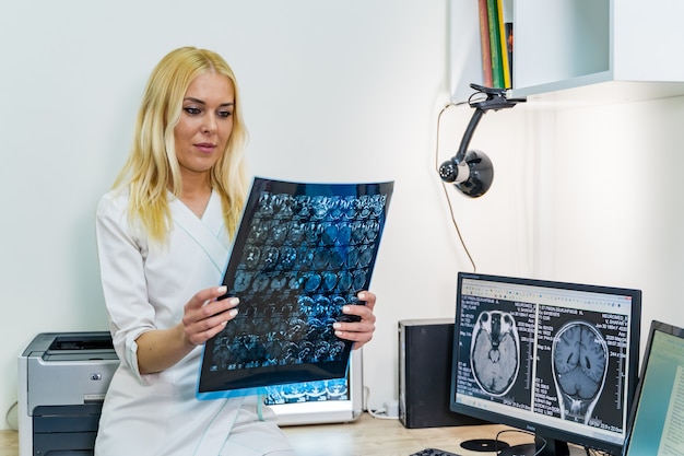 Foto doctora leyendo una imagen de rayos x cerca de la máquina de imágenes por resonancia magnética.