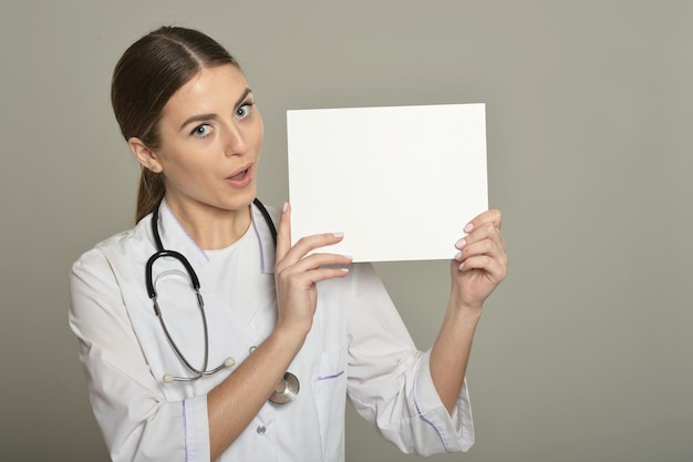 Doctora con lista blanca, de pie sobre fondo gris