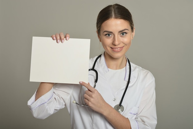 Doctora con lista blanca, de pie sobre fondo gris