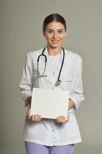 Doctora con lista blanca, de pie sobre fondo gris