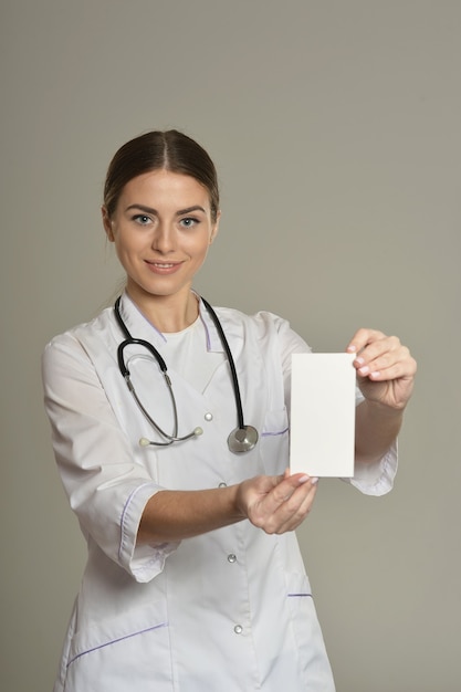 Doctora con lista blanca, de pie sobre fondo gris