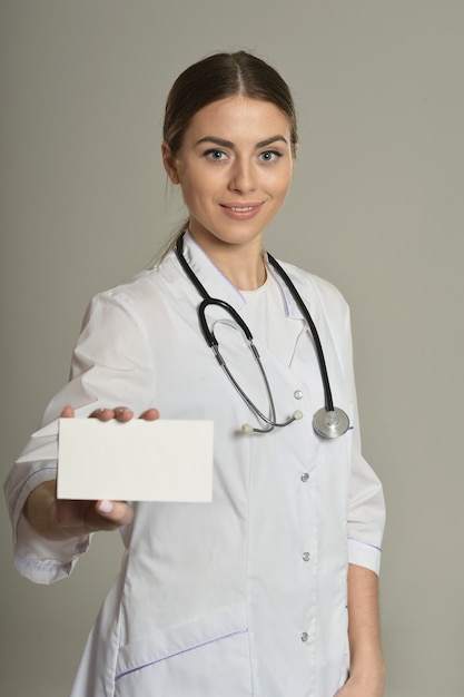 Doctora con lista blanca, de pie sobre fondo gris