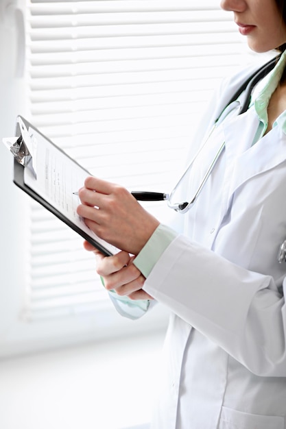 Doctora llenando el historial médico de pie cerca de la ventana en el hospital