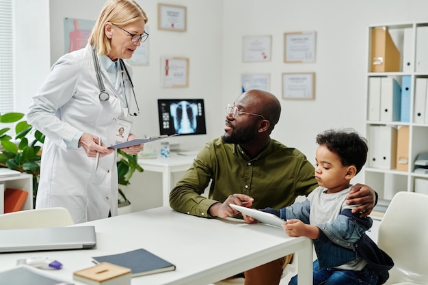 Doctora madura consultando a un joven afroamericano con un hijo pequeño