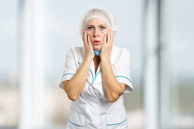 Foto doctora madura que parece sorprendida. enfermera madura sorprendida que lleva a cabo las manos en la cara y que parece preocupada, borrosa.