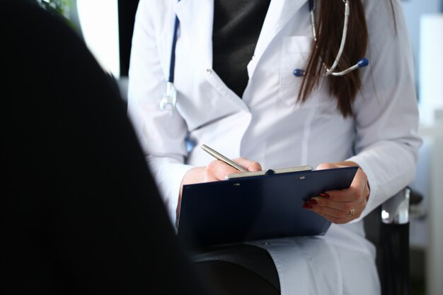 Doctora mano sostenga la pluma de plata llenando la lista de antecedentes del paciente en el portapapeles.