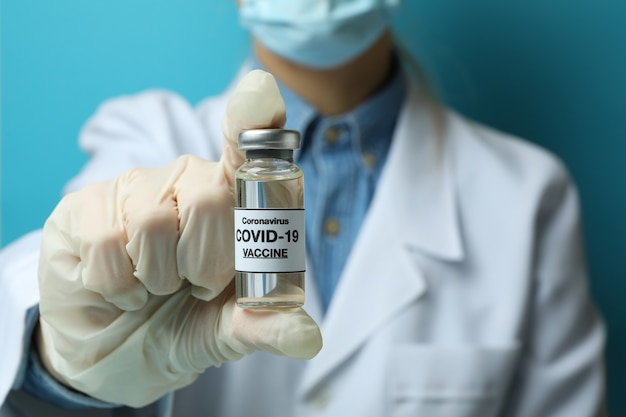 Doctora mantenga el frasco con la vacuna COVID - 19 sobre fondo azul.