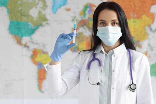 Doctora en máscara médica protectora sostiene una jeringa con vacuna en el fondo del mapa del mundo