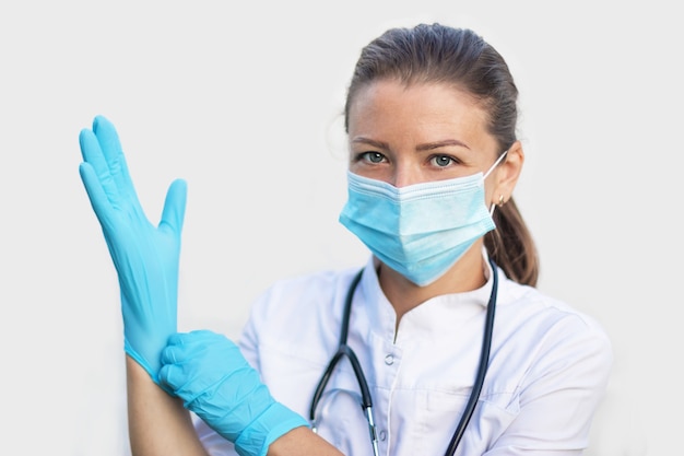 Doctora en máscara poniéndose guantes azules