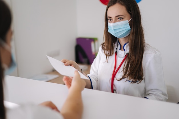 Doctora en máscara protectora dé papel con receta a cliente clínica brillante