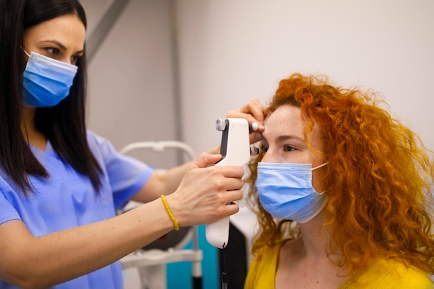 Una doctora con mascarilla examina los ojos de su cliente