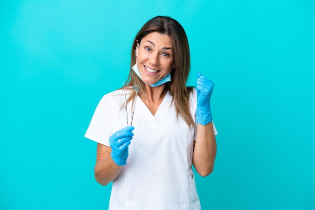 Doctora de mediana edad aislada de fondo azul celebrando una victoria en posición ganadora