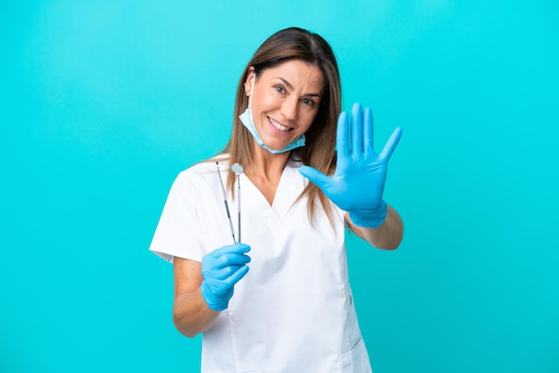 Doctora de mediana edad aislada de fondo azul contando cinco con los dedos