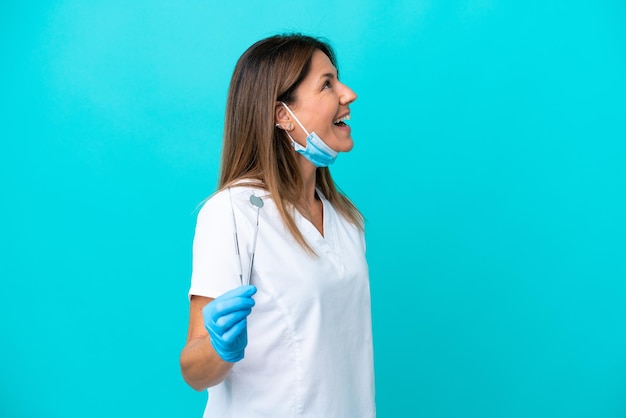 Doctora de mediana edad aislada de fondo azul riéndose en posición lateral