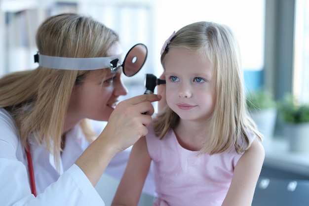 Doctora mira en el oído de una niña, primer plano. Examen médico de un niño en edad preescolar, pediatría.