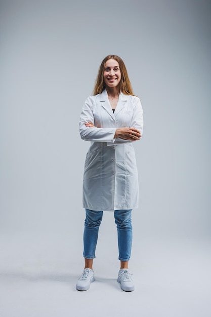 Foto doctora moderna y alegre con una bata blanca sobre un fondo gris doctora con una sonrisa en la cara