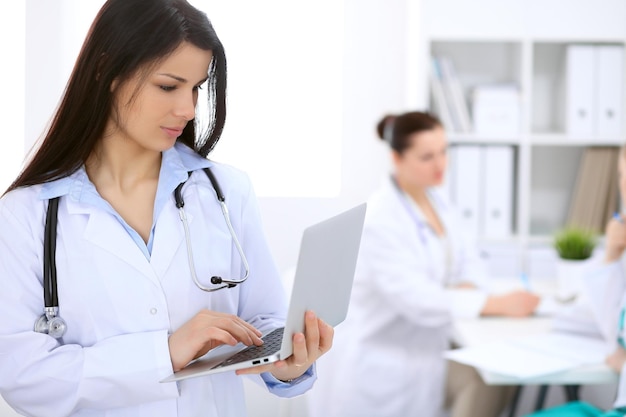 Doctora morena en el fondo de colegas hablando entre ellos en el hospital.