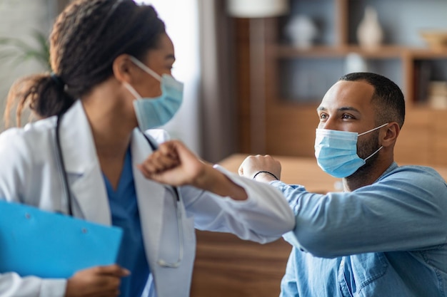 Foto doctora negra saludando a paciente varón con toque de codo