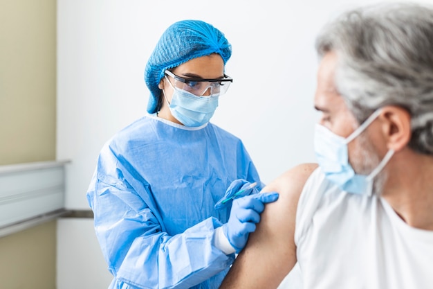 Foto doctora o enfermera dando inyección o vacuna al hombro de un paciente.