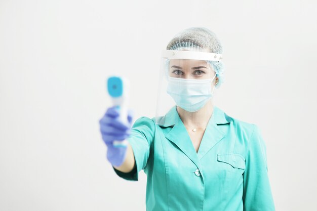 Foto doctora o enfermera en máscara protectora en el hospital tiene pirómetro en la mano