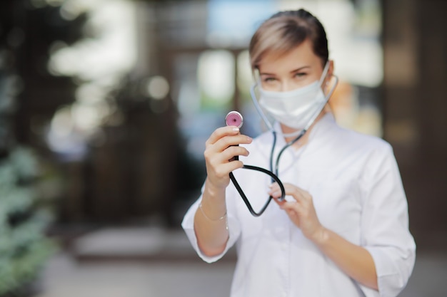 Una doctora o enfermera con una máscara protectora sosteniendo un estetoscopio en la mano