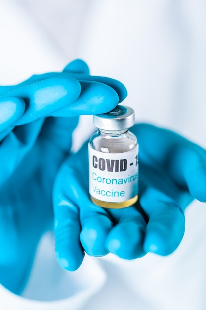 Doctora o enfermera en uniforme y guantes con mascarilla protectora en laboratorio con frasco de vacuna de vial de medicina con etiqueta de vacuna de Coronovirus COVID-19