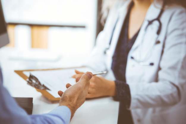 Doctora y paciente masculino discutiendo el examen de salud actual mientras están sentados en la clínica, de cerca. Concepto de medicina.