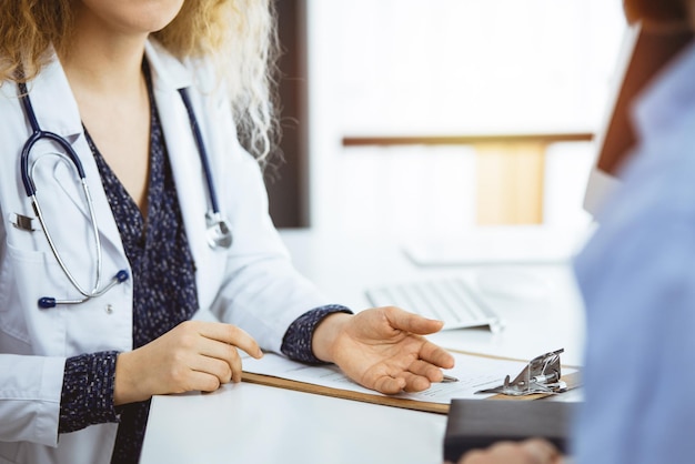 Doctora y paciente masculino discutiendo el examen de salud actual mientras están sentados en una clínica soleada, de cerca. Medicina, salud.