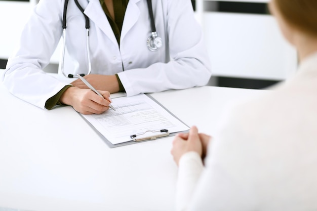 Doctora y paciente sentados y hablando en el examen médico en el primer plano de la oficina del hospital