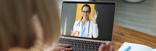 Foto doctora en la pantalla del portátil agitando la mano al paciente enfermo