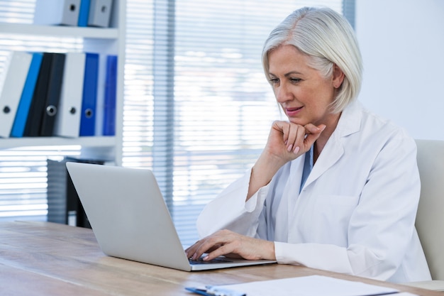 Doctora pensativa trabajando en su computadora portátil