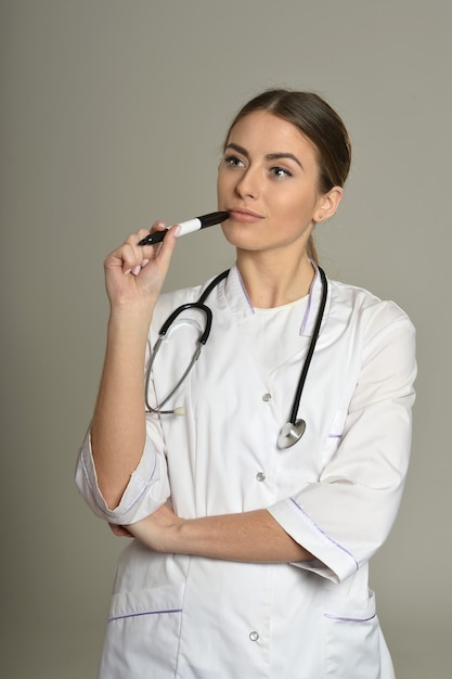 Doctora de pie con un rotulador sobre fondo gris