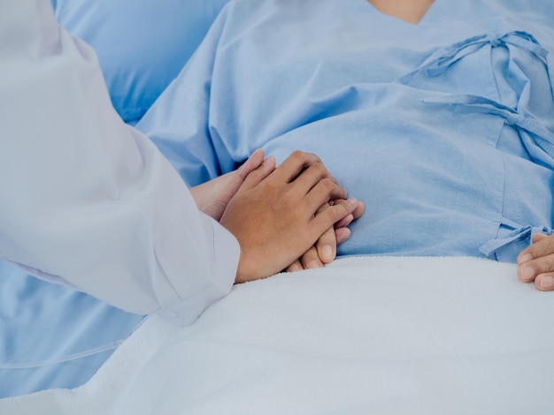 Una doctora de primer plano con traje blanco se aferra a la mano de una anciana anciana con un vestido azul claro con una manguera salina acostada en la cama del hospital alentando el concepto de paciente