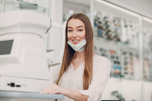 Doctora profesional con mascarilla usando pruebas oculares equipos modernos digitales electrónicos que controlan la visión